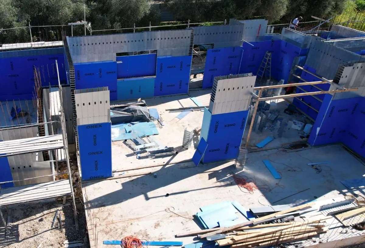 מבט אווירי רחב על אתר הבנייה עם קירות אלמנטי תבנית מורכבים ולוחות בידוד כחולים, פרויקט שתי וילות בגבעת ישעיהו