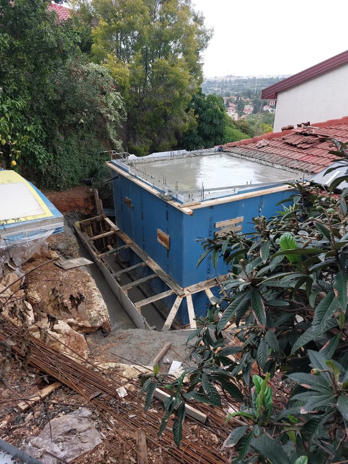 תוספת ממ"ד לבית פרטי על מדרון, יציקת בטון על גבי המודול לצד בית עם גג רעפים